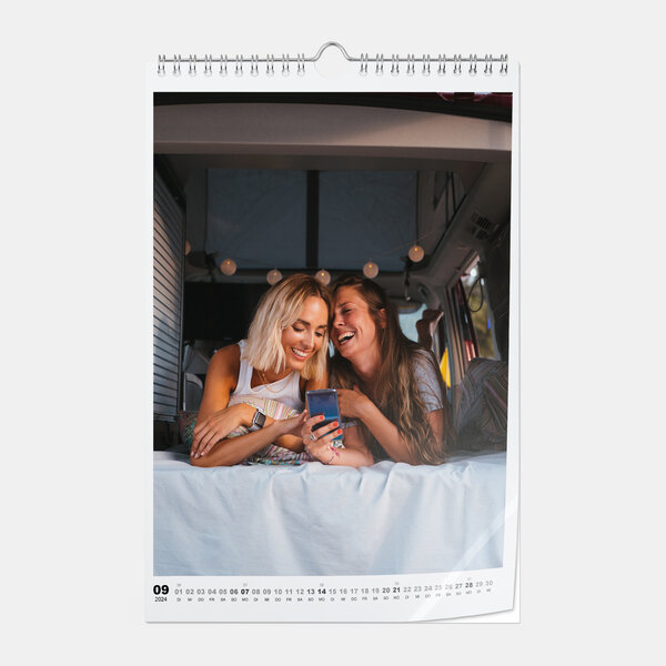 Der Fotokalender in A4-Hochformat auf glänzendem Fotopapier zeigt zwei Frauen lachend im Bett eines Campers mit Smartphone.