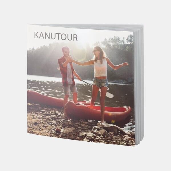 Ein quadratisches Fotobuch mit dem Titel „Kanutour“ zeigt ein junges Paar beim Einstieg ins Kanu am sonnigen Seeufer.