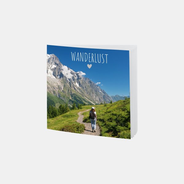 Das RUCK ZUCK Fotobuch® zeigt eine Wanderin auf einem Bergpfad mit Blick auf majestätische Alpenlandschaft im Sonnenschein.