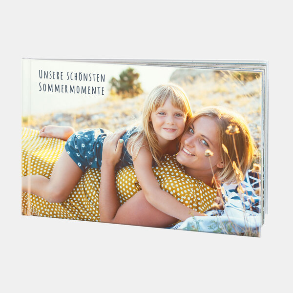 Eine Frau liegt auf einer Decke im Sommerfeld und umarmt ein Kind – ideal für personalisiertes Fotobuch mit Sommermomenten.